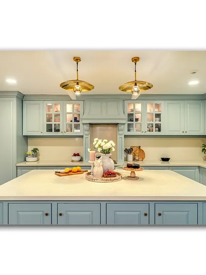 A beautiful, country-style kitchen with powder blue cabinets and a large central island. The warm brass pendant lights and carefully styled countertop create a welcoming and functional heart of the home.