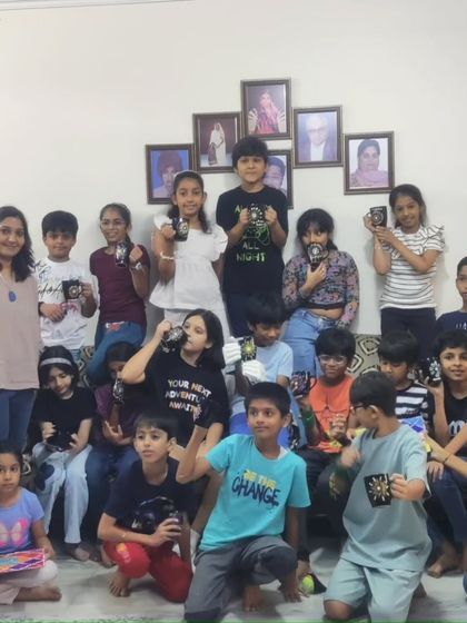 The full group of young artists from Kushagra and Geetarth's birthday party, holding up the unique dot mandala mugs they designed.