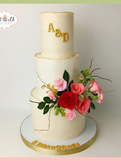A timeless three-tiered wedding cake with rustic, unfinished edges. It's decorated with a simple yet beautiful arrangement of fresh flowers and a custom monogram.