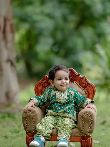 Dressed in a handsome green traditional outfit, this little boy takes a moment on his throne. The soft natural light and serene expression make this a wonderfully peaceful and classic child portrait.