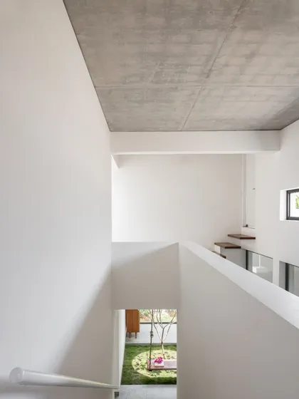 Looking down from the first floor into the central courtyard, this view reveals the home's vertical connection. The exposed concrete ceiling and crisp white walls are part of our simple, durable, and cost-effective material palette.