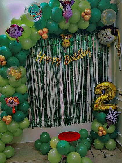 A simple but fun jungle-themed balloon arch for a second birthday. This setup uses a green foil curtain, animal-shaped balloons, and a large number '2' foil balloon.
