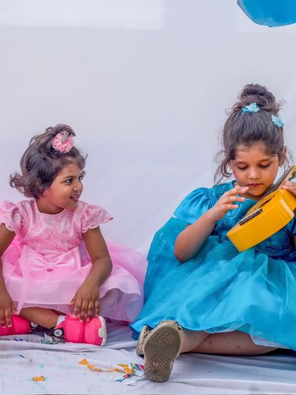Sisterly love and party-ready style. One sister wears a dreamy pink tulle dress while the other shines in a vibrant blue, both ready to play and make music together.