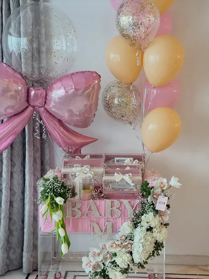 Welcoming a baby girl with all the elegance she deserves. This stunning acrylic hamper features personalized pearl lettering, designer gifts, and a cascade of fresh flowers, all tied together with a beautiful pink bow.