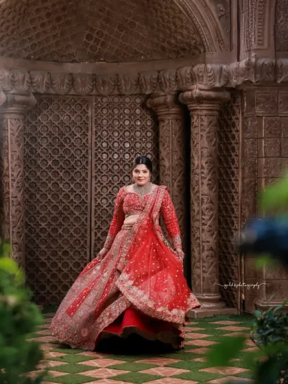 This shot captures the bride amidst lush greenery, with the vibrant red of her lehenga standing out beautifully. The movement in the skirt adds a dynamic and celebratory feel.