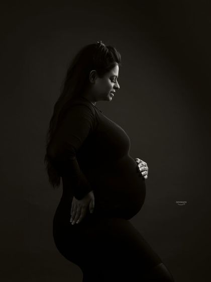 A classic low-key portrait in black and white. The lighting is carefully shaped to sculpt the client's form, creating a timeless and intimate image that focuses on the beauty of her pregnancy.