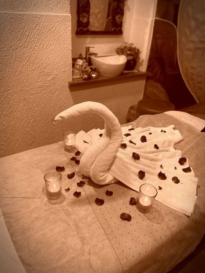 It's all in the details. A freshly prepared treatment bed adorned with a towel swan, delicate petals, and soft candlelight. This is the welcome that awaits you, setting the stage for a session of pure pampering and relaxation.