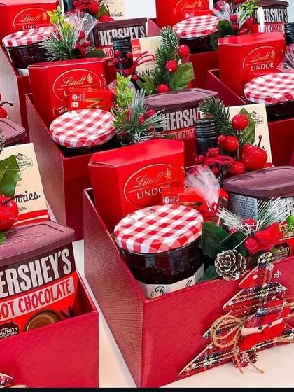 Our 2024 Christmas hampers in festive red boxes. These are filled with cozy treats like Hershey's Hot Chocolate, Lindt chocolates, and cookies.