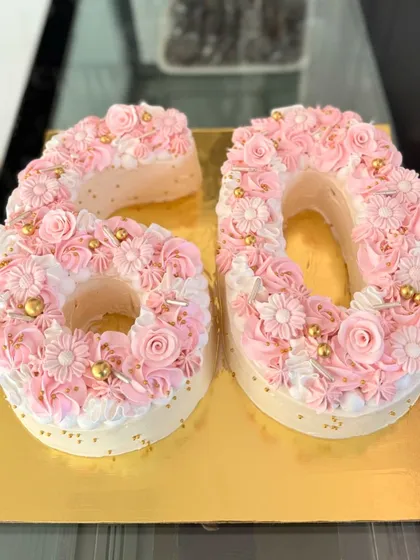 Celebrating a 60th birthday in style with a beautiful monogram cake. Each number is delicately decorated with pink and white buttercream flowers and shimmering gold sprinkles for an elegant and personal touch.