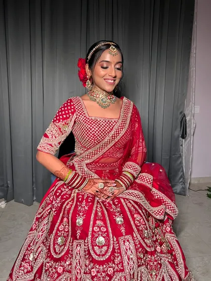 A smiling bride seated, her magnificent red lehenga spread out beautifully.