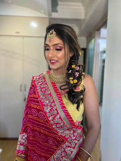 A beautiful Mehendi look featuring a traditional Bandhani dupatta. The makeup is bright and festive, with a fun, floral braided hairstyle.
