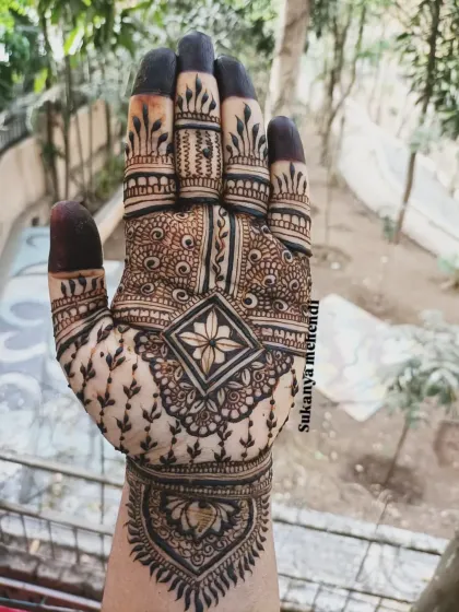 A striking single-hand design with a central floral diamond pattern, surrounded by delicate vine work. The filled fingertips add a traditional touch.