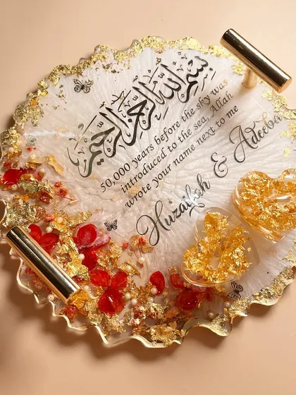 A beautiful round ring tray in white, red, and gold. It features a Quranic verse and heart-shaped ring holders filled with gold leaf.