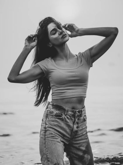 A beautiful, serene moment captured in monochrome. The model's pose is relaxed and natural against the backdrop of the sea.