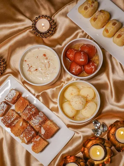A festive tabletop arrangement of Indian sweets, including gulab jamun and rasgulla, styled with golden fabric and lit diyas. This is an example of my food photography for seasonal campaigns and brand promotions.