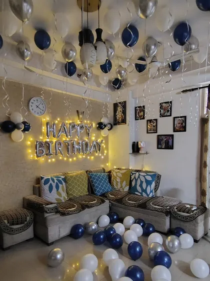 A living room birthday surprise in blue, white, and silver. I used balloons on the ceiling and floor, and a 'Happy Birthday' banner with fairy lights.