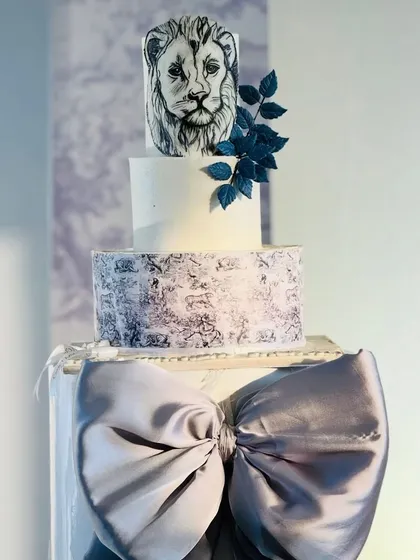 A masterpiece of a cake, perfectly matching the theme with a hand-drawn lion, a large grey bow, and a subtle toile pattern.