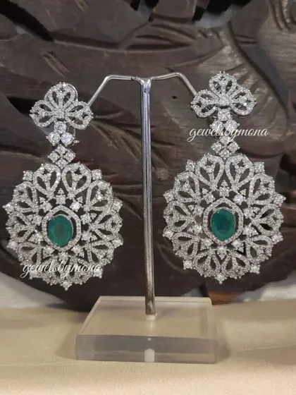 These large, ornate diamond earrings are crafted for making an impact. Centered with a beautiful emerald and surrounded by an intricate web of diamonds, they are perfect for completing a royal bridal look.