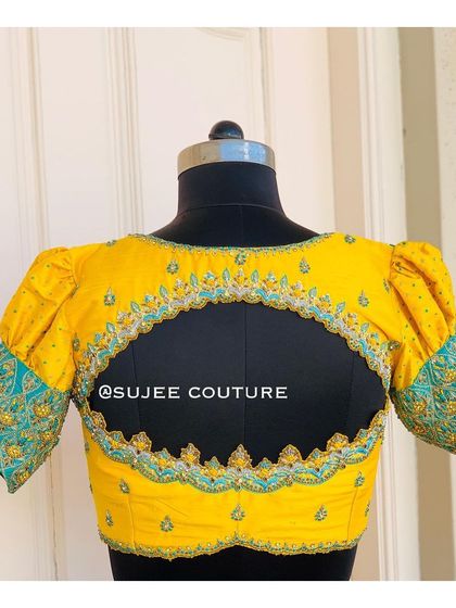 A bright yellow blouse with puff sleeves and a contrasting teal embroidered cuff. The back features a large keyhole cutout, framed with intricate zardozi and beadwork.