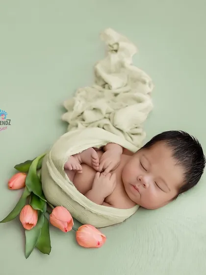 Wrapped snugly with delicate tulips, this pose is all about elegance. The simple green background makes the soft pink of the flowers and the baby's wrap pop.