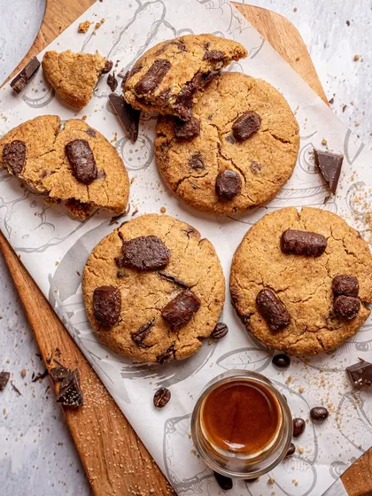 A flatlay of freshly baked chocolate chunk cookies. The scattered crumbs and coffee beans create a rustic, homemade feel. This top down shot is great for showing texture and context.
