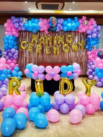 A Frozen-themed naming ceremony decoration. The setup uses pink and blue balloons with foil letters spelling out 'NAMING CEREMONY'.