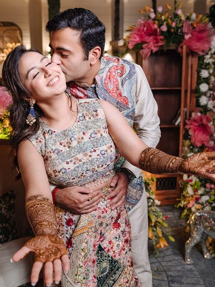 A happy, candid moment of the groom kissing his bride's cheek as she shows off her beautiful henna.
