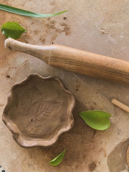 A hand-built bowl with a leaf impression, next to the rolling pin used to make it. A beautiful connection to nature.