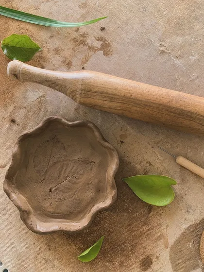 A hand-built bowl with a leaf impression, next to the rolling pin used to make it. A beautiful connection to nature.