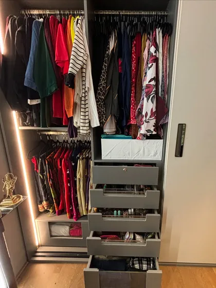 A sliding door wardrobe opened to reveal multiple sections for hanging clothes and a bank of drawers for accessories.