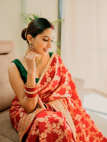 A classic bridal portrait in a red Banarasi saree. The makeup is timeless, with a neat bun, defined eyes, and a red bindi.
