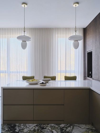 A view of the kitchen during the sunset. The combination of natural light from the large windows and the stylish pendant lights over the island creates an absolutely serene retreat.