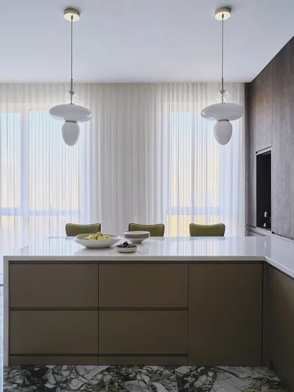 A view of the kitchen during the sunset. The combination of natural light from the large windows and the stylish pendant lights over the island creates an absolutely serene retreat.