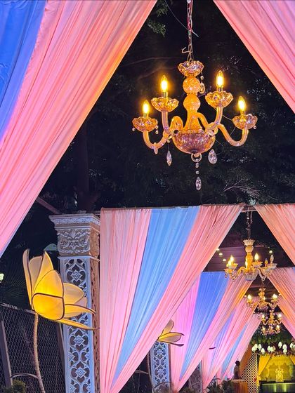 A close-up of the pastel-themed entrance, highlighting the warm glow of the chandelier against the pink and blue drapes. The lit lotus flowers on the pillars add a unique, artistic touch.