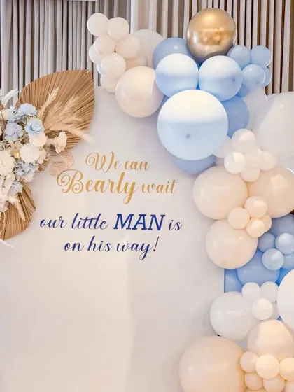 The details make the difference. This close-up shows the custom vinyl text "We can Bearly wait, our little MAN is on his way!" on a clean white backdrop, framed by a balloon garland and dried floral accents for a rustic touch.