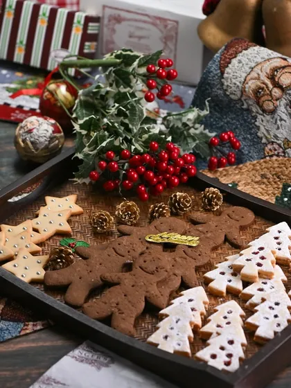 A Christmas cookie platter ready for a celebration. It features our classic gingerbread men, jam-filled tree cookies, and star-shaped butter cookies, arranged beautifully on a wooden tray.