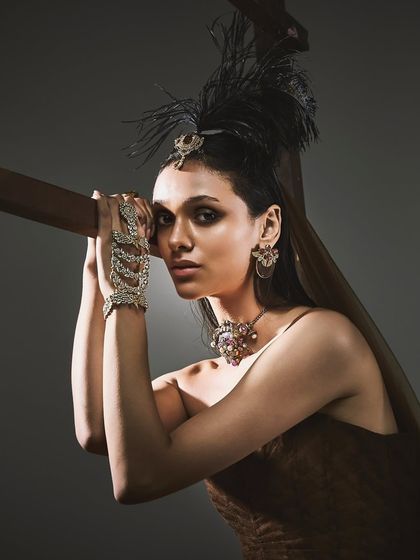 A portrait for Reasons Jewellery's "Regal Dusk" collection, featuring a model with a feather headpiece and a multi-gemstone necklace, creating a look of sophisticated royalty.