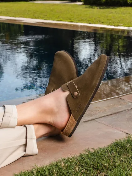 A poolside shot focusing on a pair of suede clogs. The image captures a moment of leisure and comfort, associating the product with relaxation and effortless style.