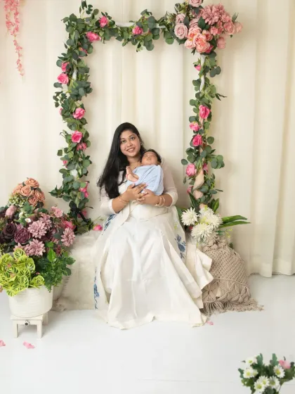 A wide shot showing the beautiful floral arch setup as a mother sits and holds her newborn baby.
