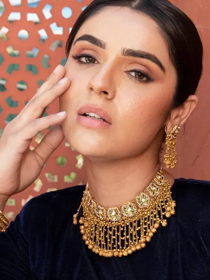 A close-up beauty shot from a jewellery campaign. The model is wearing a traditional gold choker with intricate details, styled with a deep blue velvet top for a rich, royal look suitable for any wedding celebration.