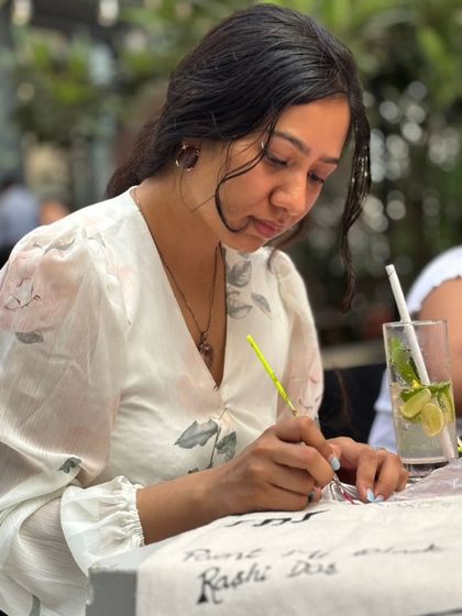 A participant carefully personalizes a tote bag with her name and design. Our tote bag painting workshops let you create a stylish and functional accessory.
