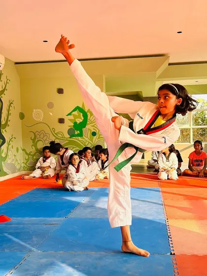 A clean, high side kick executed with perfect form and balance. The other students watch and learn, creating a supportive training environment.