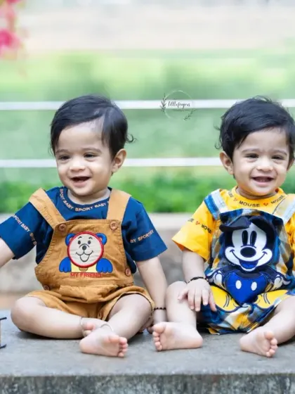 Two adorable twin baby boys sitting side by side during their outdoor photoshoot, surrounded by fun props like books and a globe. Double the smiles, double the fun.