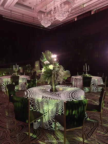 A dining table draped in a bold, black-and-white polka dot cloth, paired with emerald green velvet chairs, showcasing a playful yet sophisticated approach to event styling.