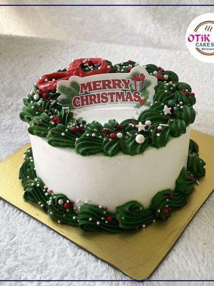 A larger Christmas wreath cake, with detailed green piping and festive red and white sprinkles, ready to be the centerpiece of your celebration.