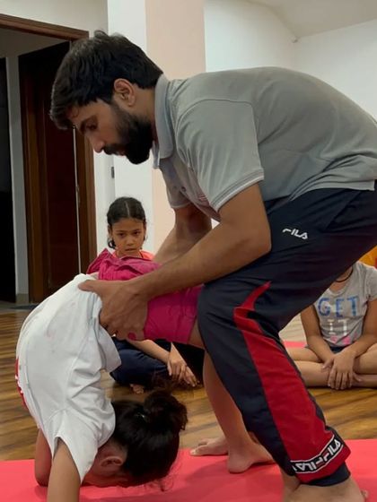 A teacher helps a young student into a backbend, demonstrating the personalized attention we provide in our kids' classes.