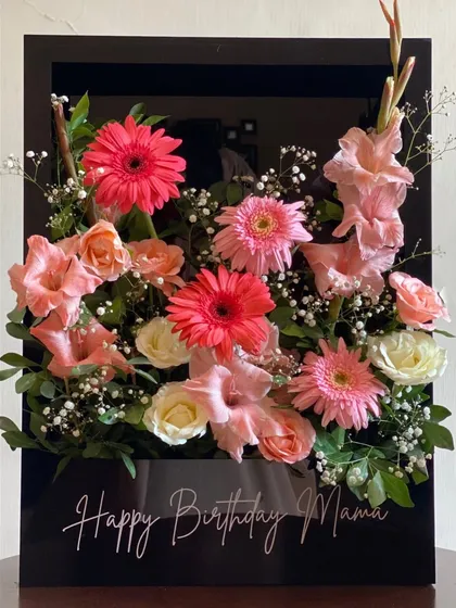 Modern elegance defined. This stunning arrangement features pink gerberas, gladioli, and soft roses in a sleek, black acrylic box with a personalized "Happy Birthday Mama" message, creating a truly luxurious statement piece.