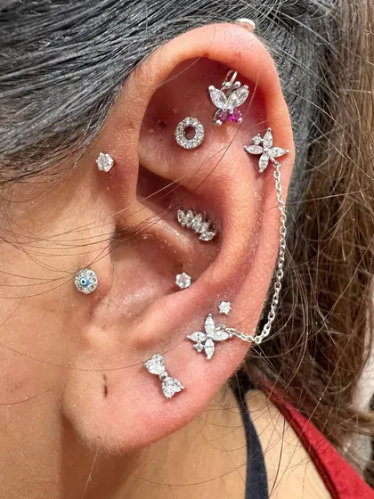 A vibrant and playful ear stack with a mix of floral studs, chains, and a butterfly hanging.