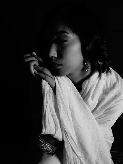 A close-up black and white portrait with a focus on texture and shadow. The light grazes across the model's face and the fabric of her scarf, creating a gentle and artistic composition.