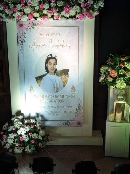 A personalized welcome stand for the First Holy Communion, featuring a beautiful photo of Aviva. The sign is framed with soft floral arrangements and lanterns, creating a heartfelt and elegant welcome.